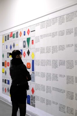 Person steht vor Wand, an der sich geometrische Symbole und Texte befinden.